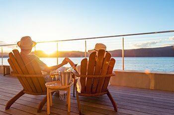 holding hands in chairs by water and sunrise